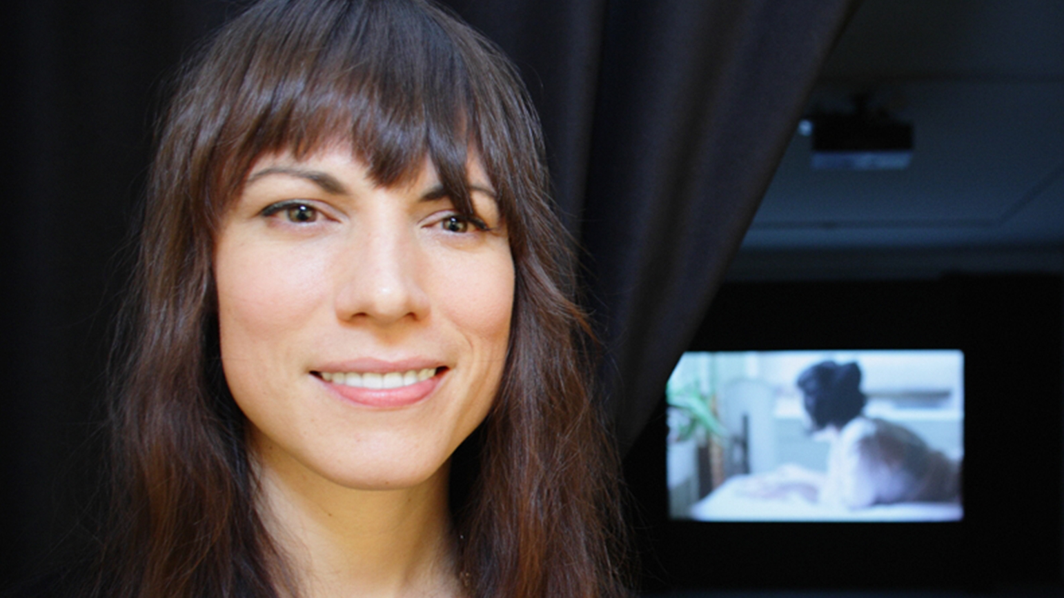 Portrait of Carrie Schneider in front of a video projection of Reading Women