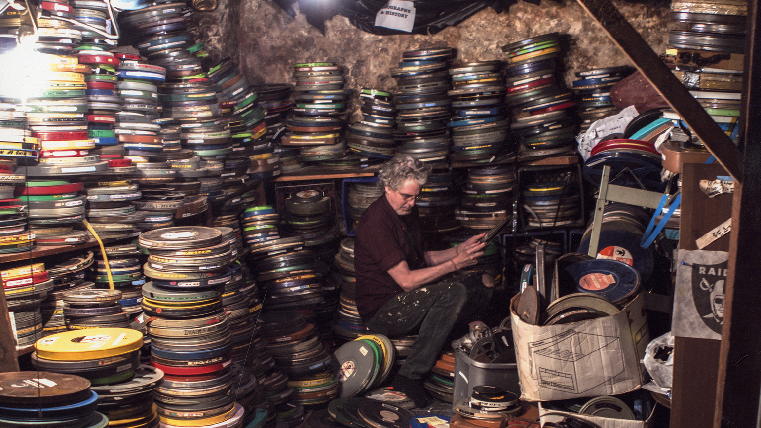 Photograph of a man sitting surrounded by stacks of film reels