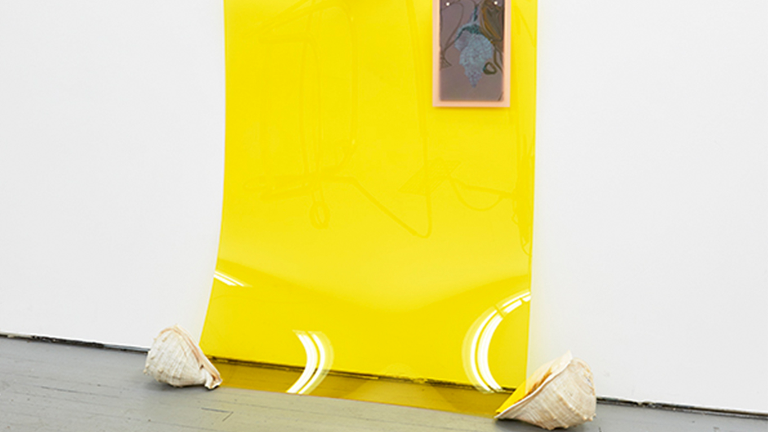 Image of artwork by Las Hermanas Iglesias, showing a large transparent yellow sheet leaning against a wall with conch shells.