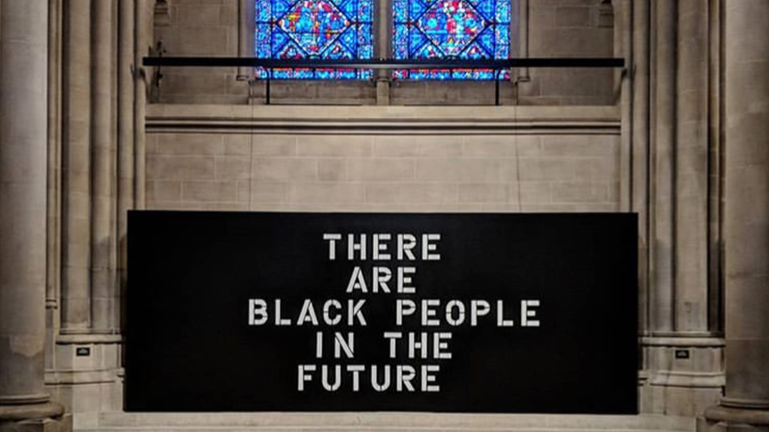 Photograph of a black sign reading "There are Black People in the Future" installed under a stained glass window in a church