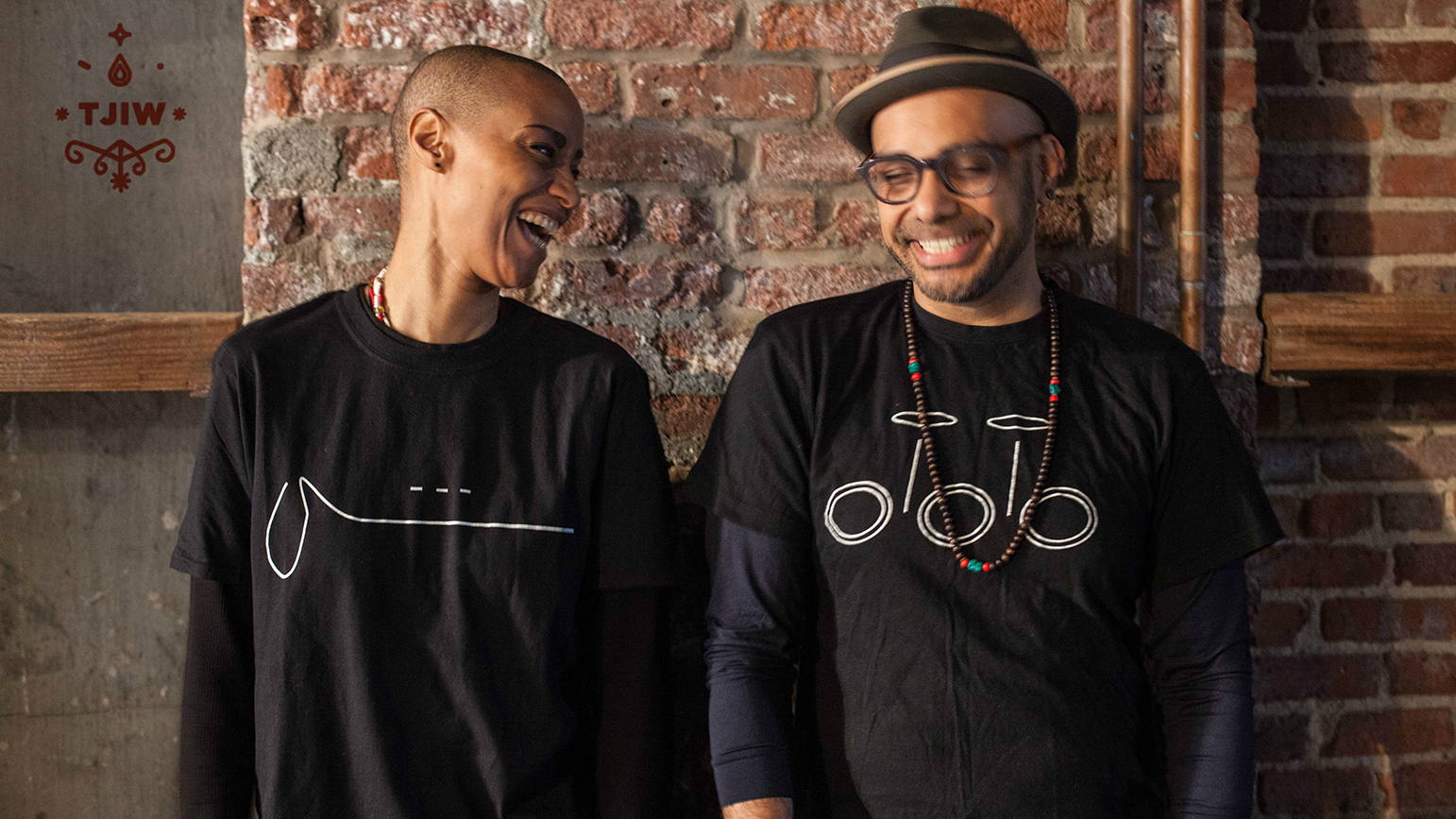 Photograph of two people laughing standing against a brick wall