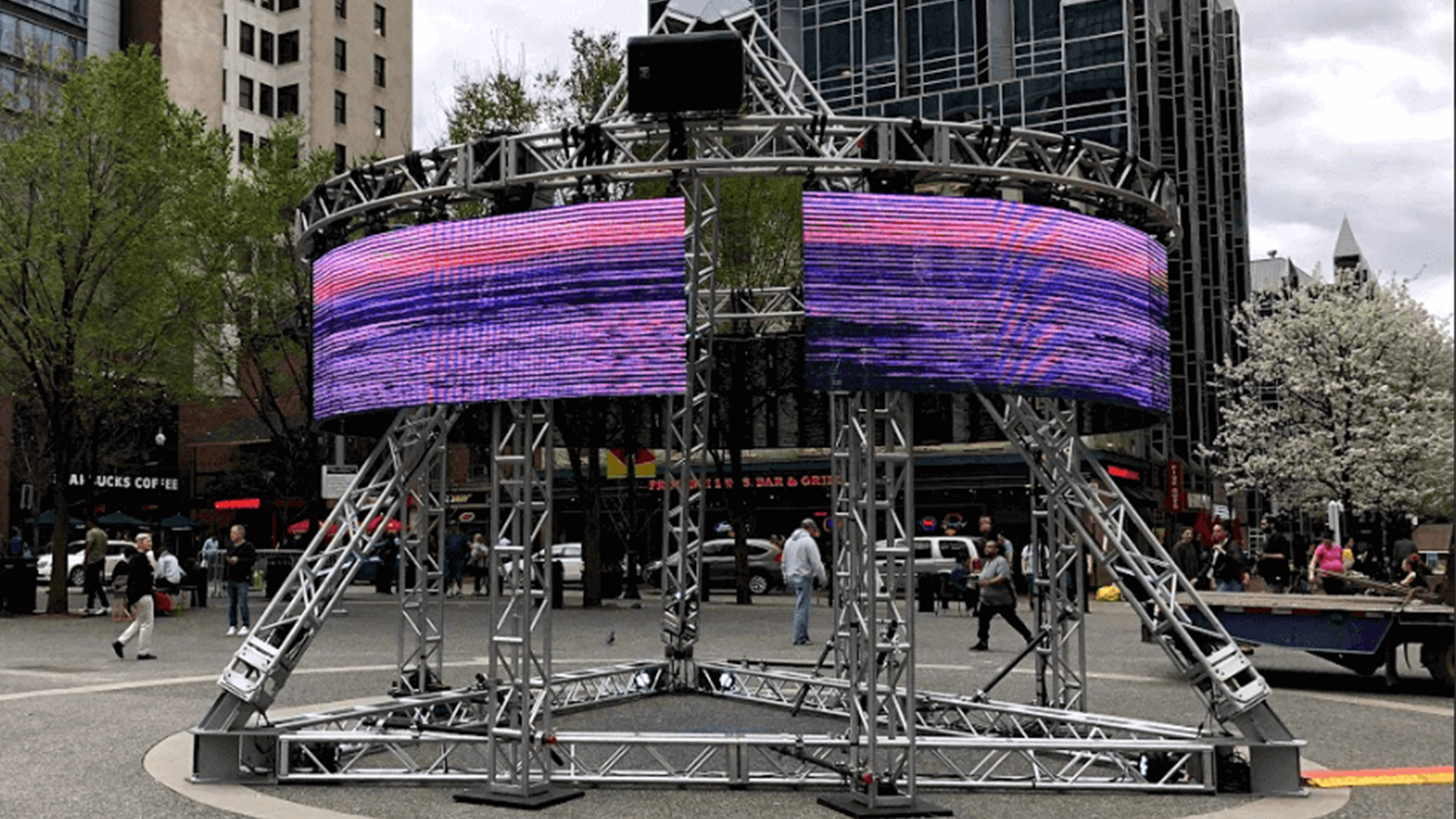 Image of circular video screens on a pyramid structure installed in a the middle of a public square