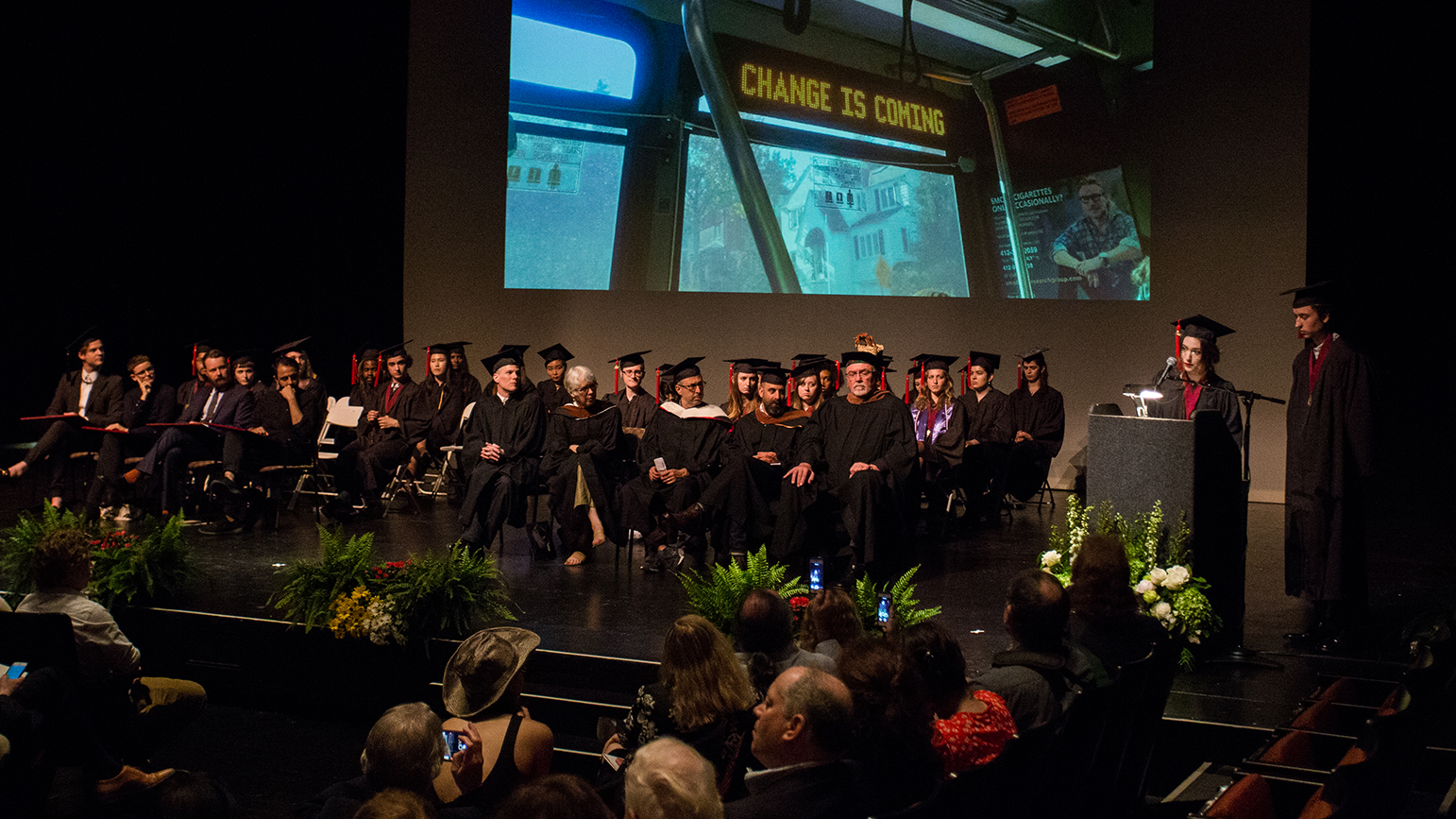 Image of graduating students in cap and gowns sitting on a stage