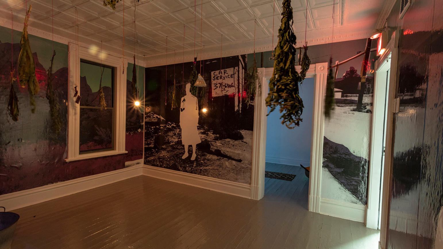 Photograph of an art installation with the walls covered in an abstracted urban landscape and dried plants having from the ceiling