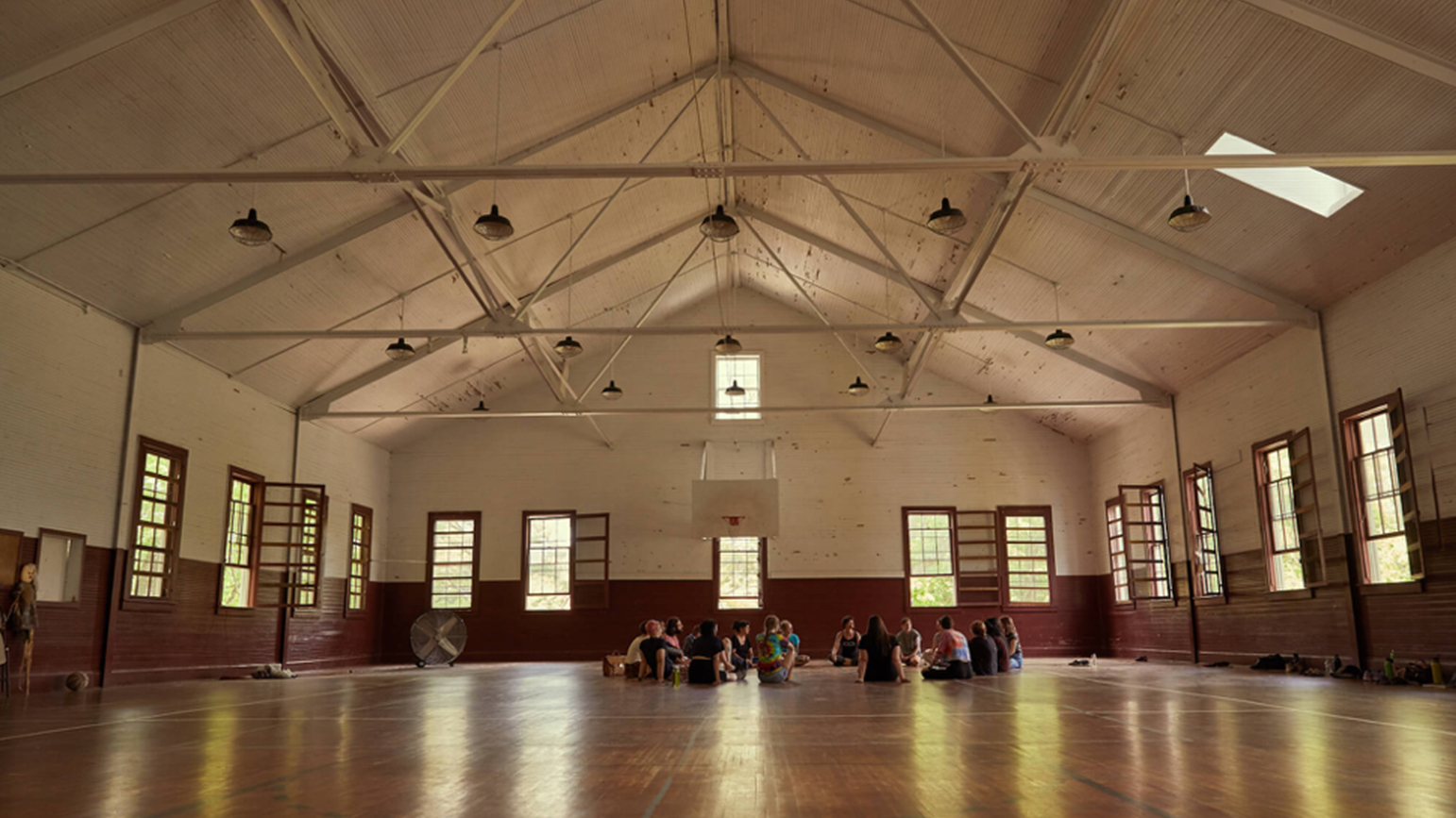 A group of people sitting in a circle on the floor of a large gymnasium