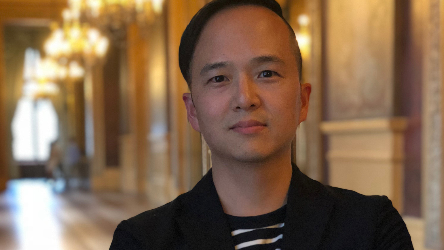 Headshot of a man standing in front of an ornate hallway