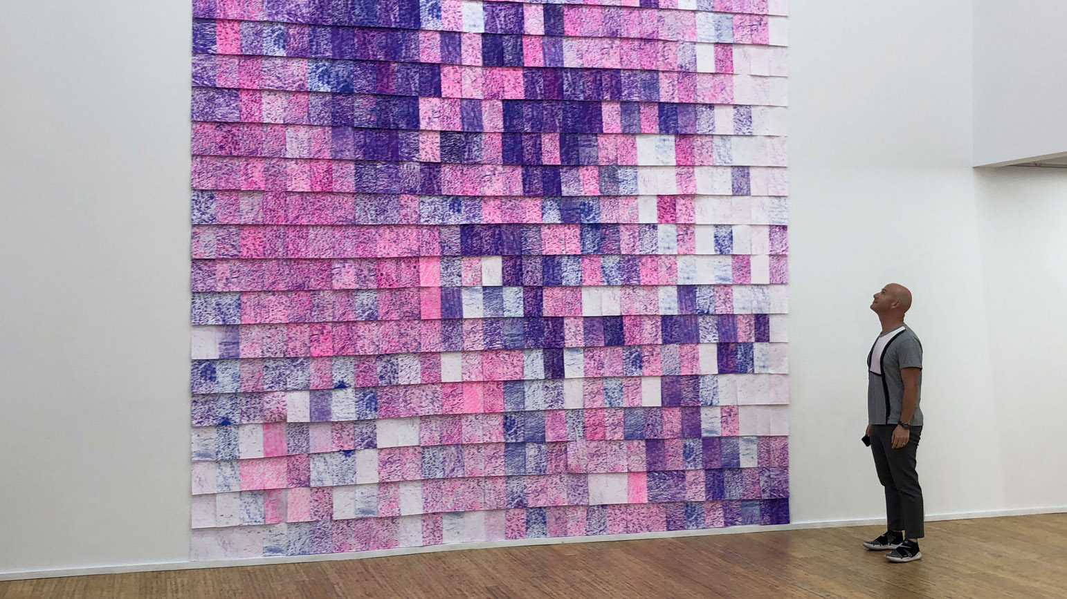 Photograph of a man looking at a large installation of blue and pink sheets of rubbings of road texture