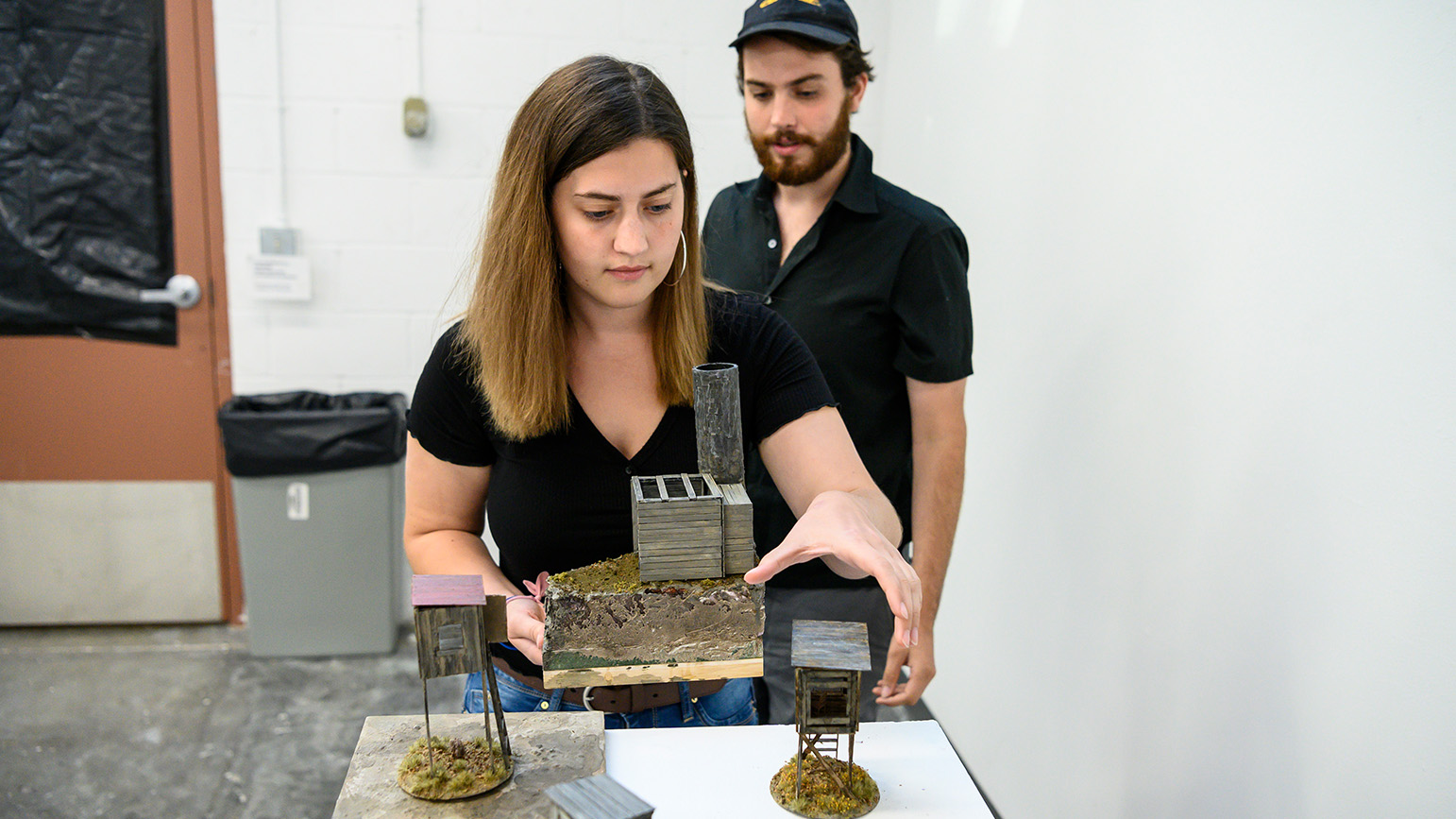 Two people setting up tabletop deer stands on a pedestal in a gallery