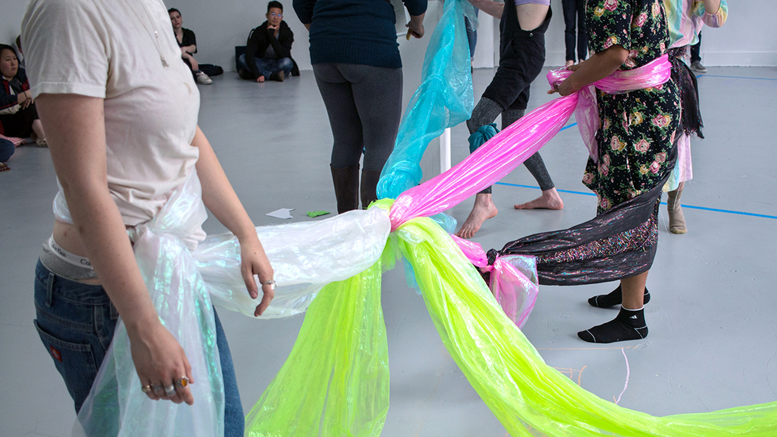A group of people connected at the waste by brightly colored fabric