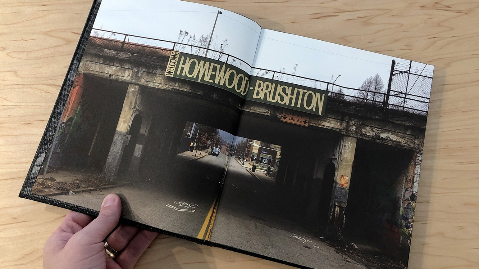 Open book with a two-page photograph spread showing an overpass with a sign with the words "Homewood Brushton"