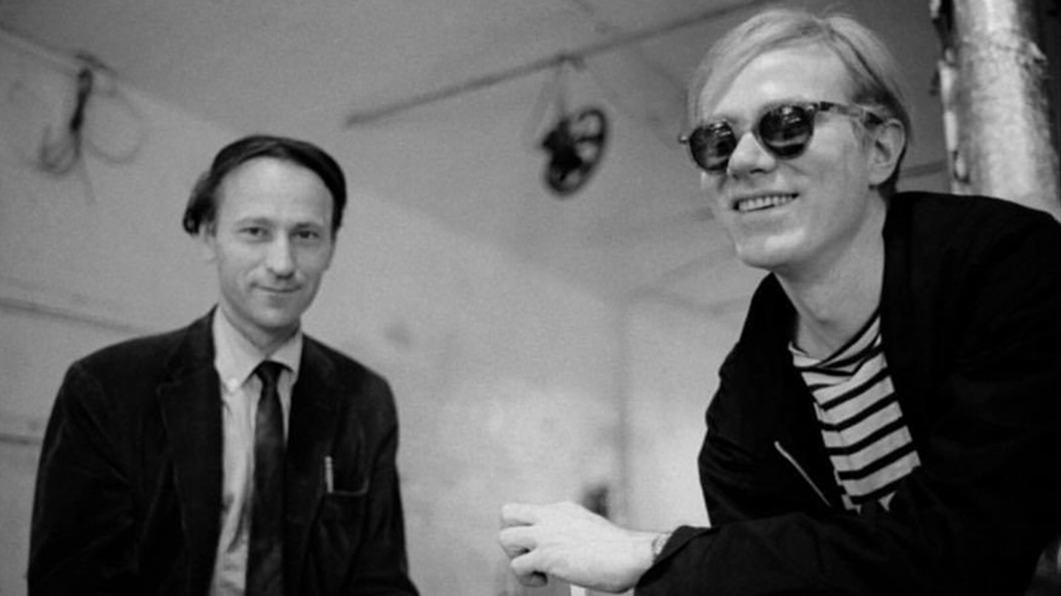 Black and white photograph of two men sitting: Jonas Mekas and Andy Warhol