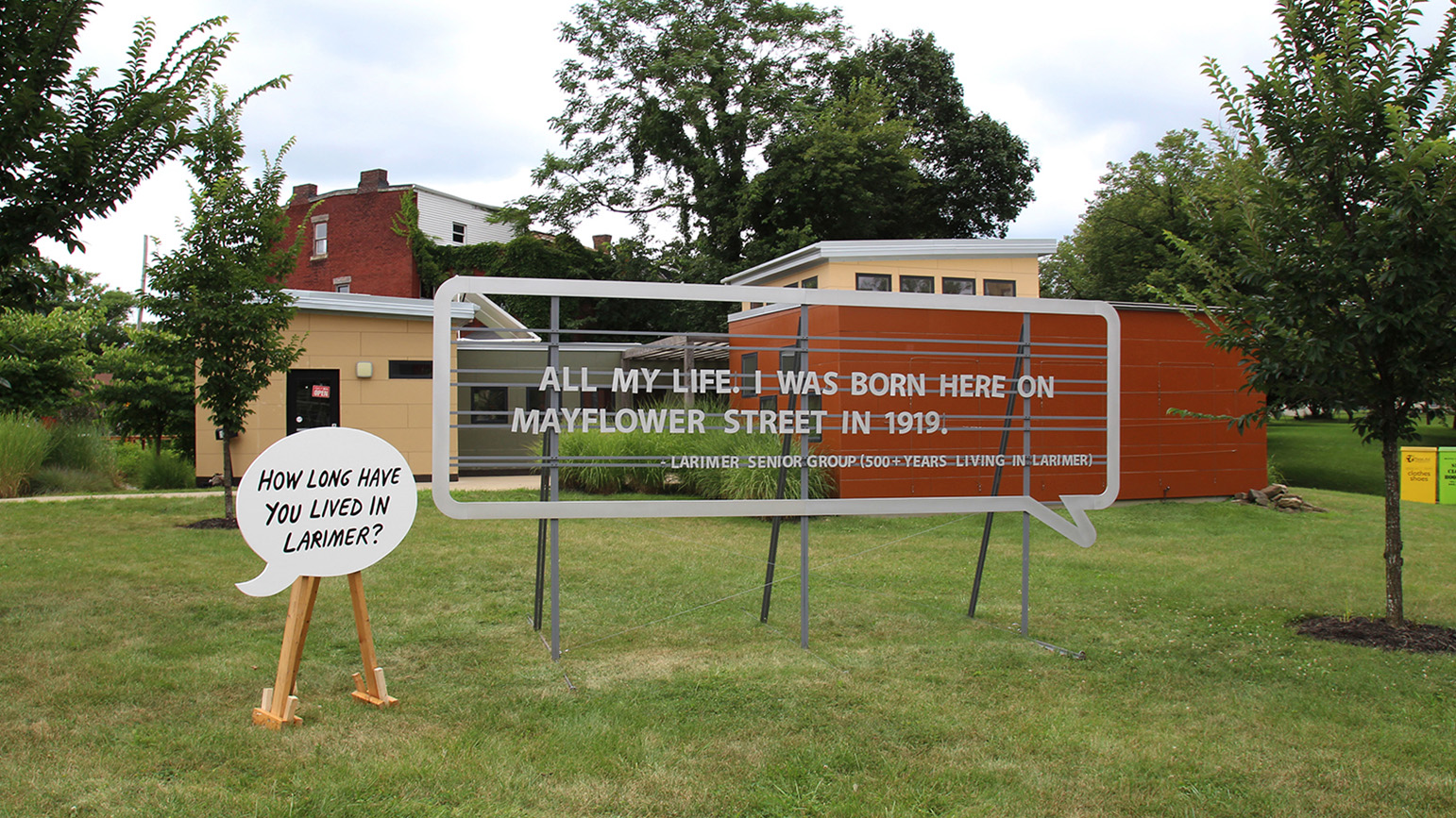 Two large speech bubbles installed outside, one reading "How long have you lived in Larimer" and the other reading "All my life. I was born here on Mayflower Street in 1919."
