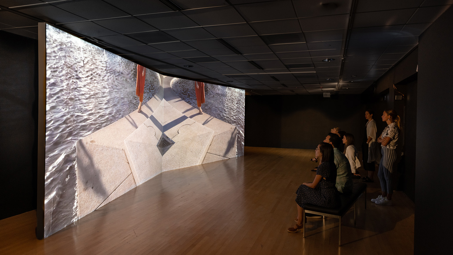 People in a gallery watching a projection on a massive screen