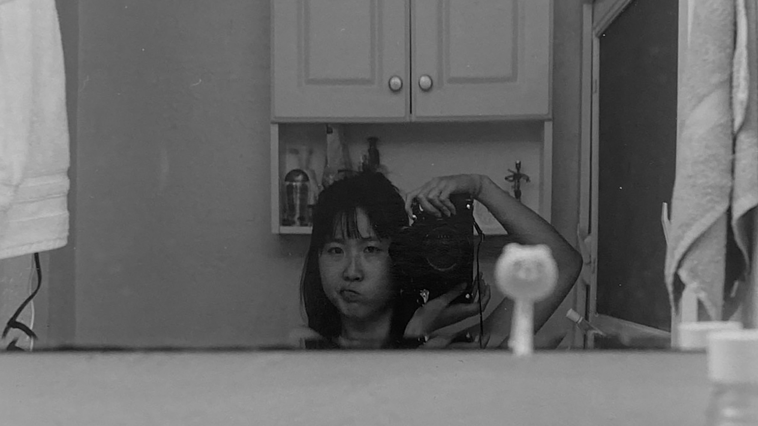 Black and white photograph of Diane Lee taken in a bathroom mirror