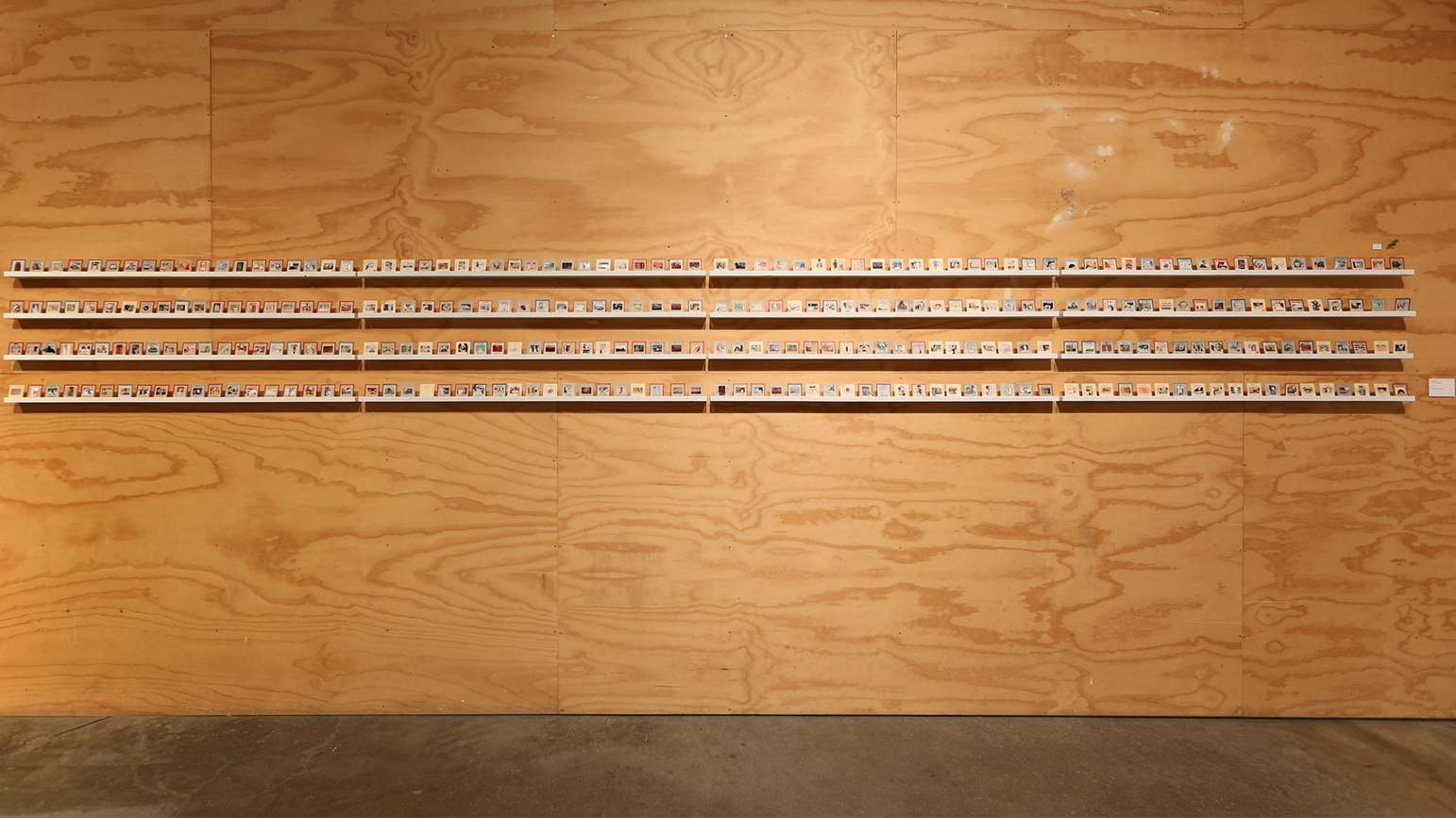 Installation view of "300 non-instagrams" showing four long shelves with 300 collages the size of film slides