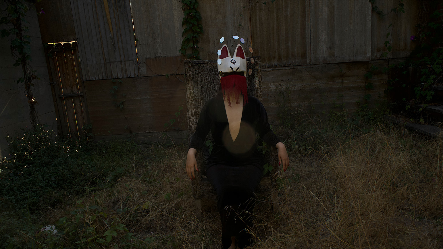 Still from a video showing a masked figured in a darkened fenced in area