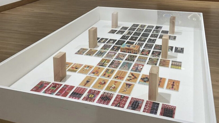 Photograph of a glass-top table in a gallery with a set of Tarot cards neatly arranged under the glass.